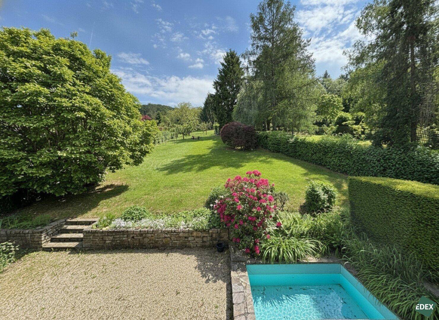 Weitläufiger grüner Garten mit Rasenfläche, Sträuchern und einem kleinen Poolbereich, ideal zum Entspannen.