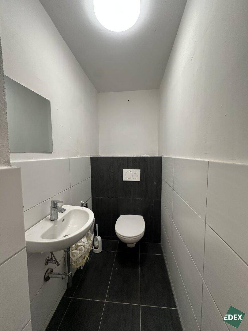 Kleine, moderne Toilette mit Waschbecken, Wand-WC und schwarz-weißen Fliesen an Wänden und Boden.