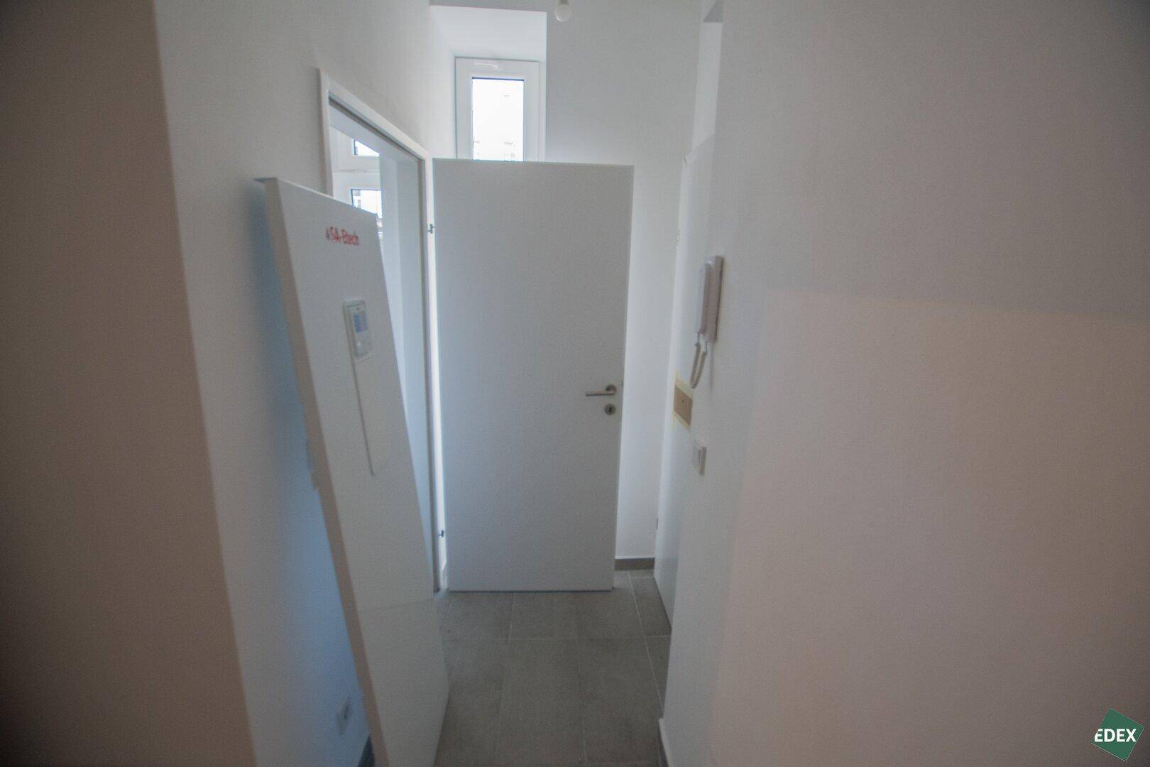 Heller Flur mit Fliesenboden, Gegensprechanlage und einem großen Heizsystem an der Wand.