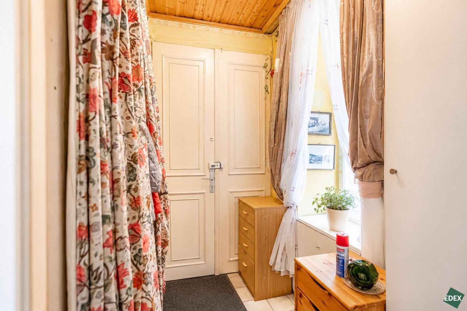 Eingangsbereich mit Holztür, Holzdecke und floralen Vorhängen, der einen warmen Empfang bietet.
