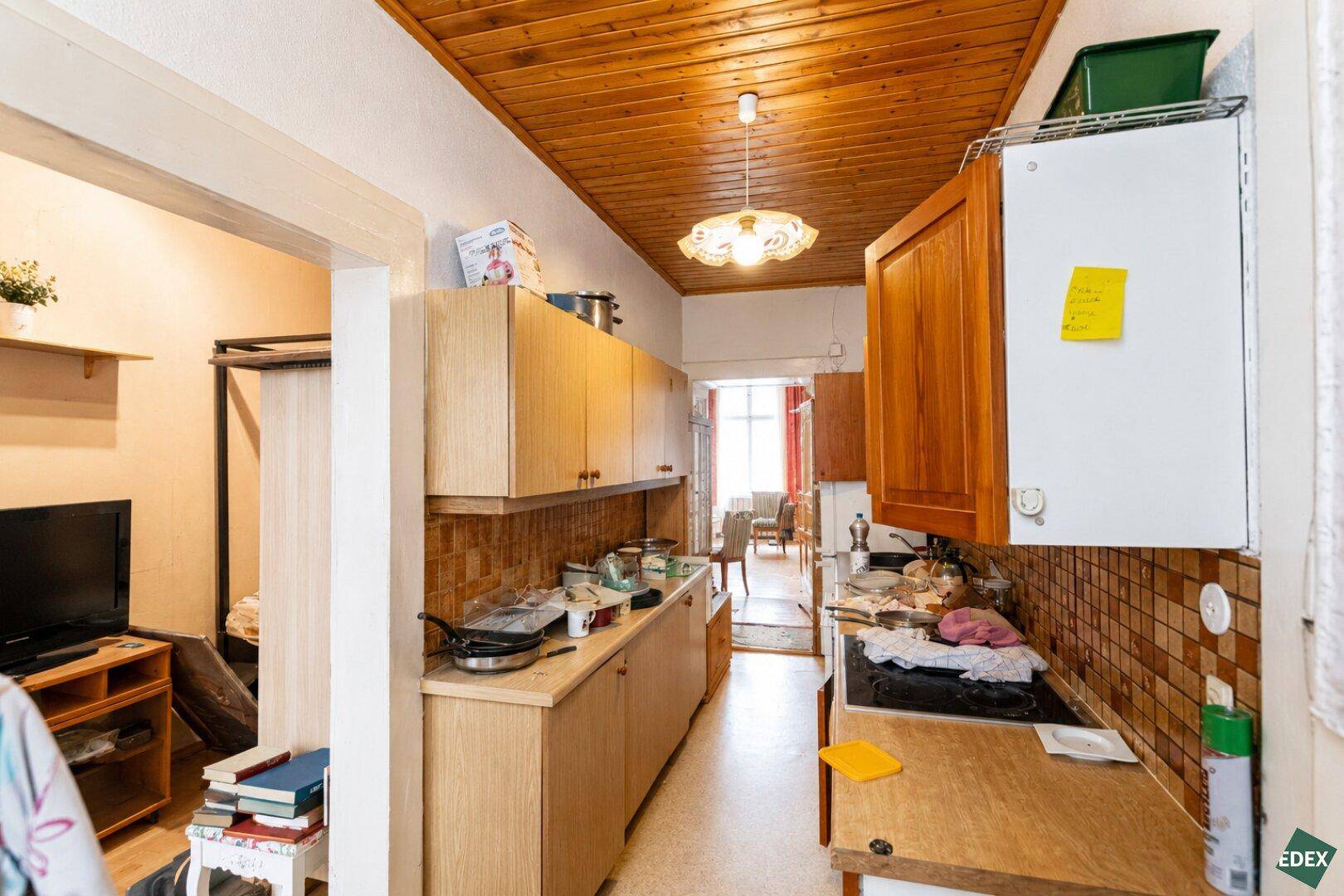 Schmale Küche mit Holzschränken, gefliestem Spritzschutz und Blick in den Essbereich.