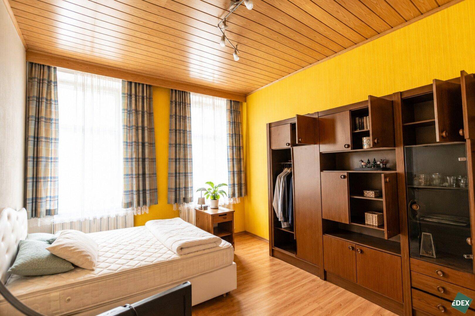 Helles Schlafzimmer mit gelben Wänden, Holzdecke und einem großen Kleiderschrank.