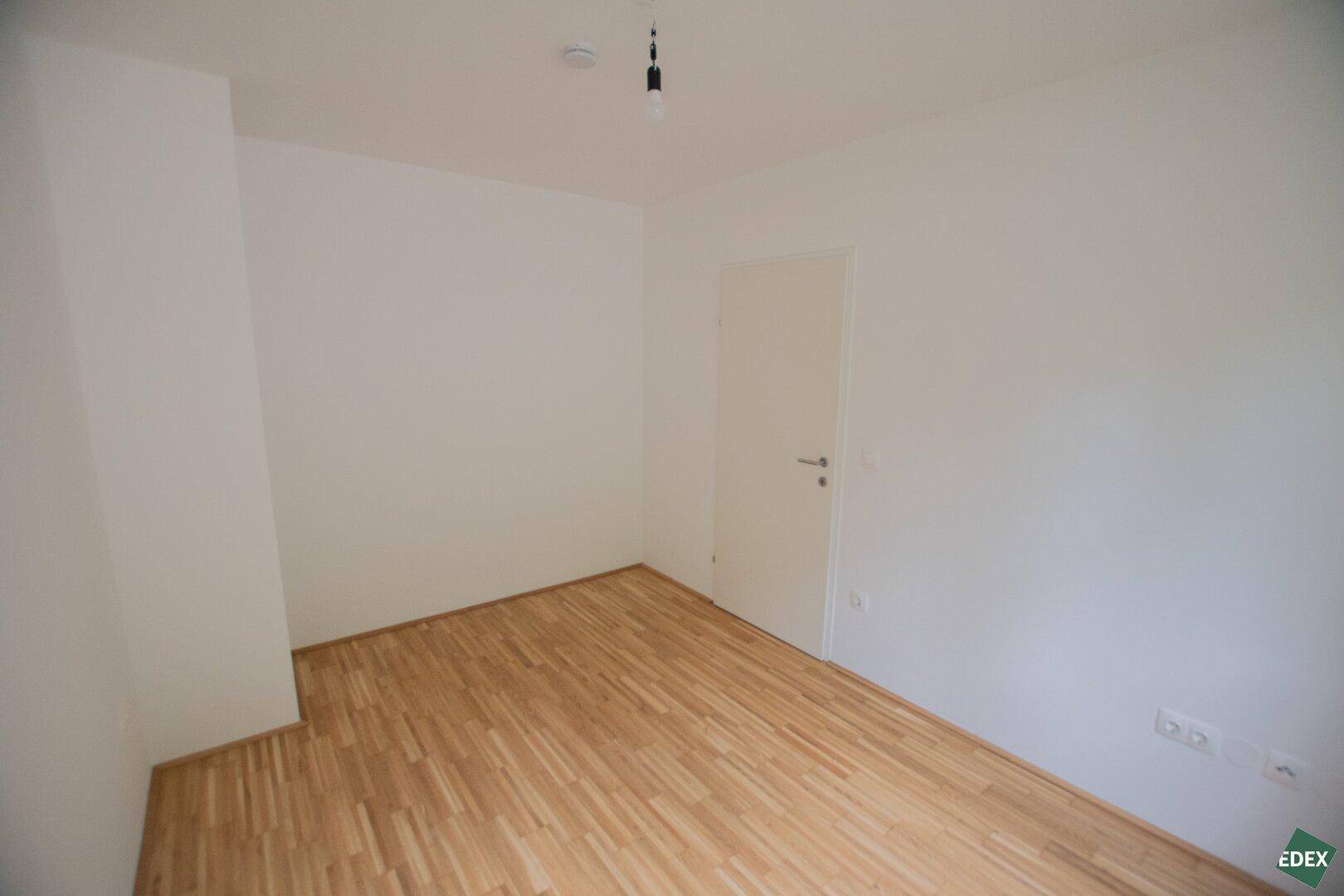 Freundliches Zimmer mit Parkettboden und weiß gestrichenen Wänden, ideal als Schlafzimmer.