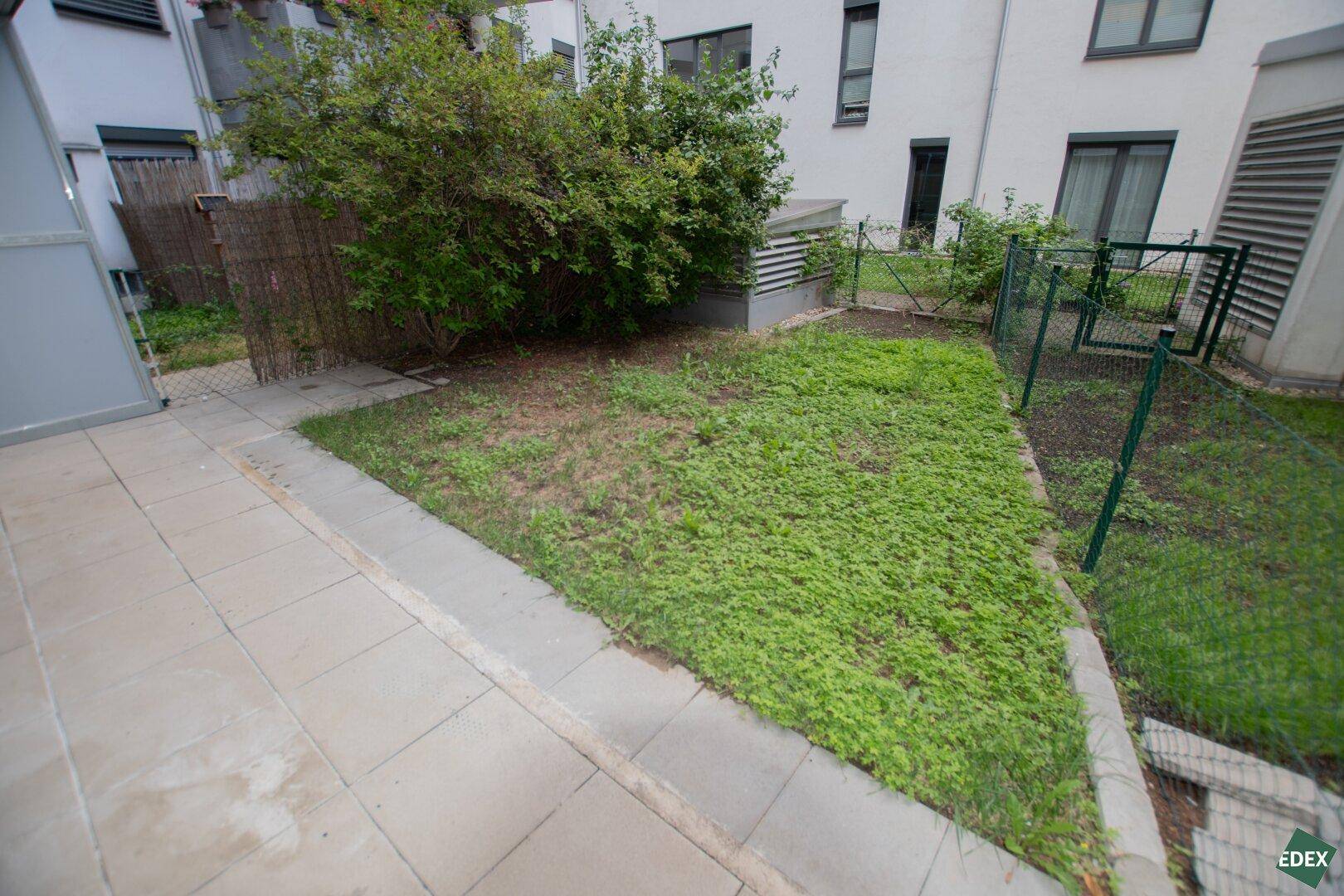 Ruhiger Gartenbereich mit Terrasse und Blick auf die umliegenden Gebäude.