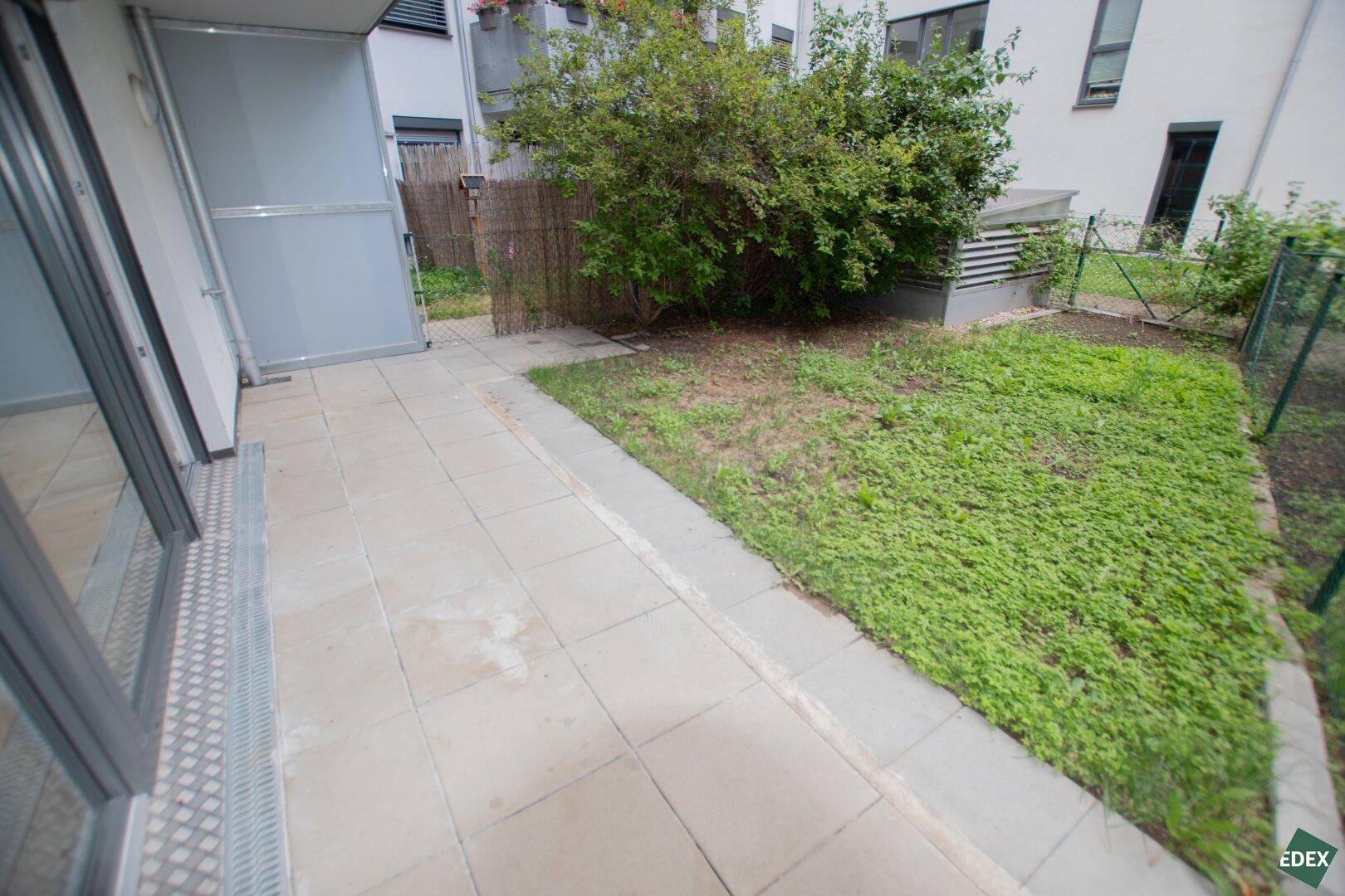 Sonniger Terrassenbereich mit Zugang zum Garten, umgeben von Grünflächen.