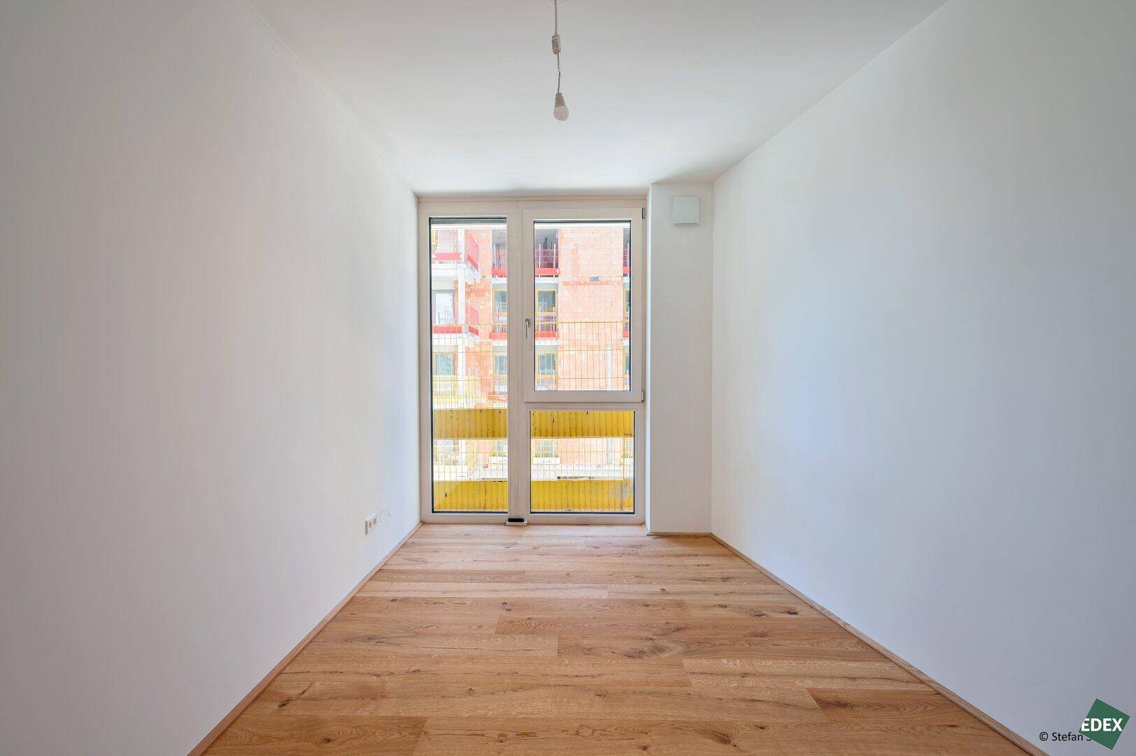 Helles Schlafzimmer mit Holzboden und Zugang zu einem Balkon, ideal für Ruhe und Entspannung.