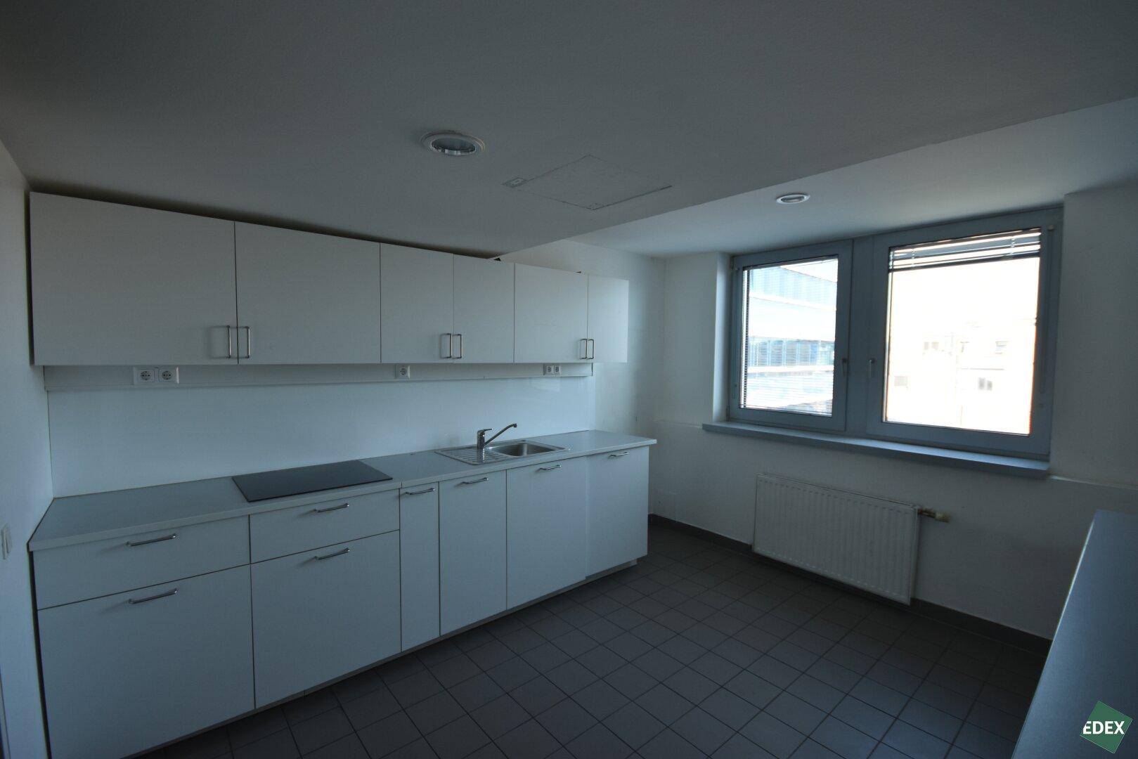 Funktionale Küchenzeile mit weißen Schränken, Spüle und Kochfeld, ausgestattet mit einem Fenster.