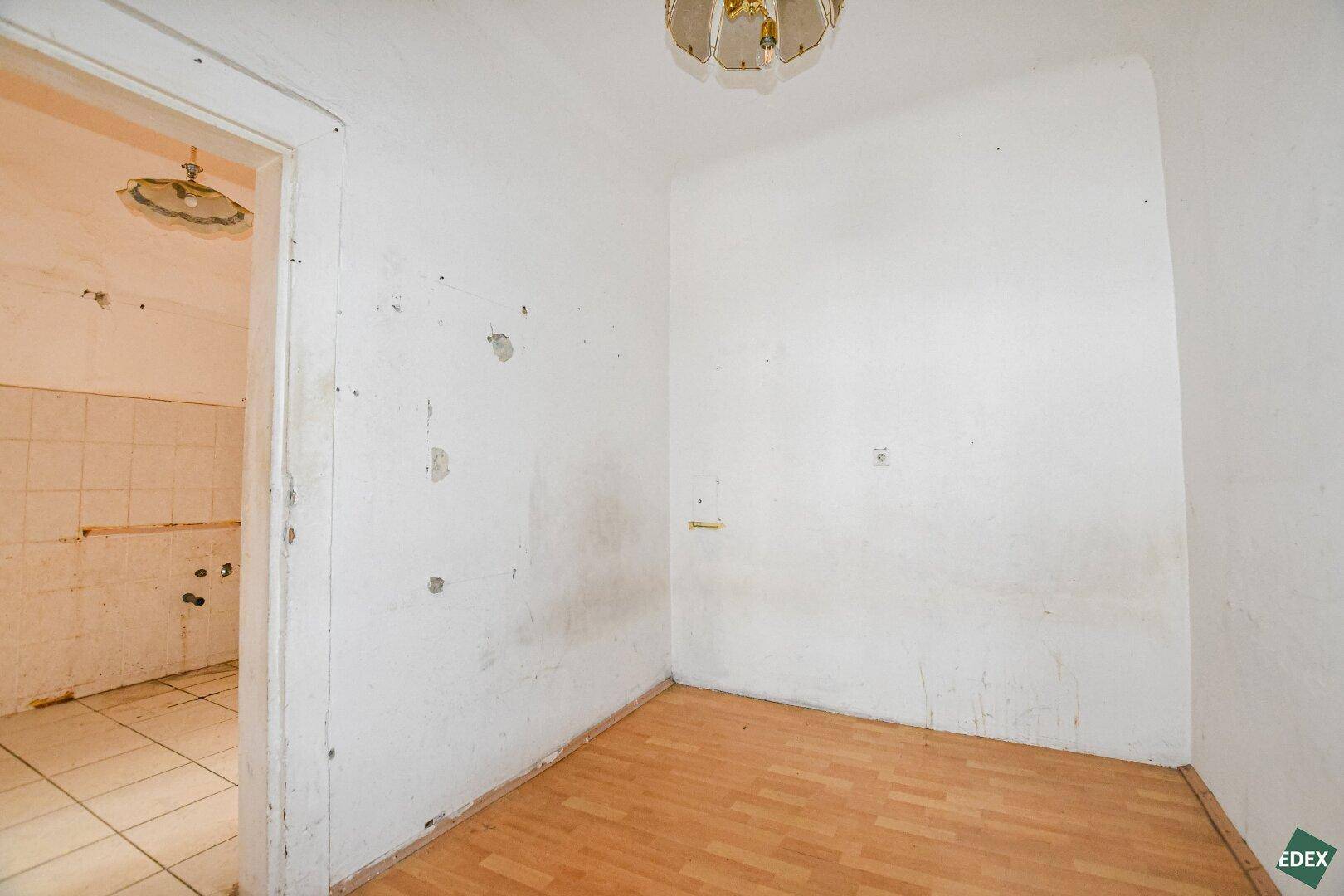 Leerer Raum mit Holzboden und Zugang zu einem gefliesten Bereich mit Wasseranschlüssen.