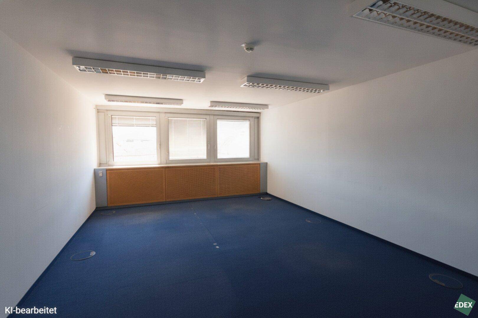 Helles, leeres Büro mit blauem Teppichboden und einer Reihe von Fenstern, die Tageslicht hereinlassen.