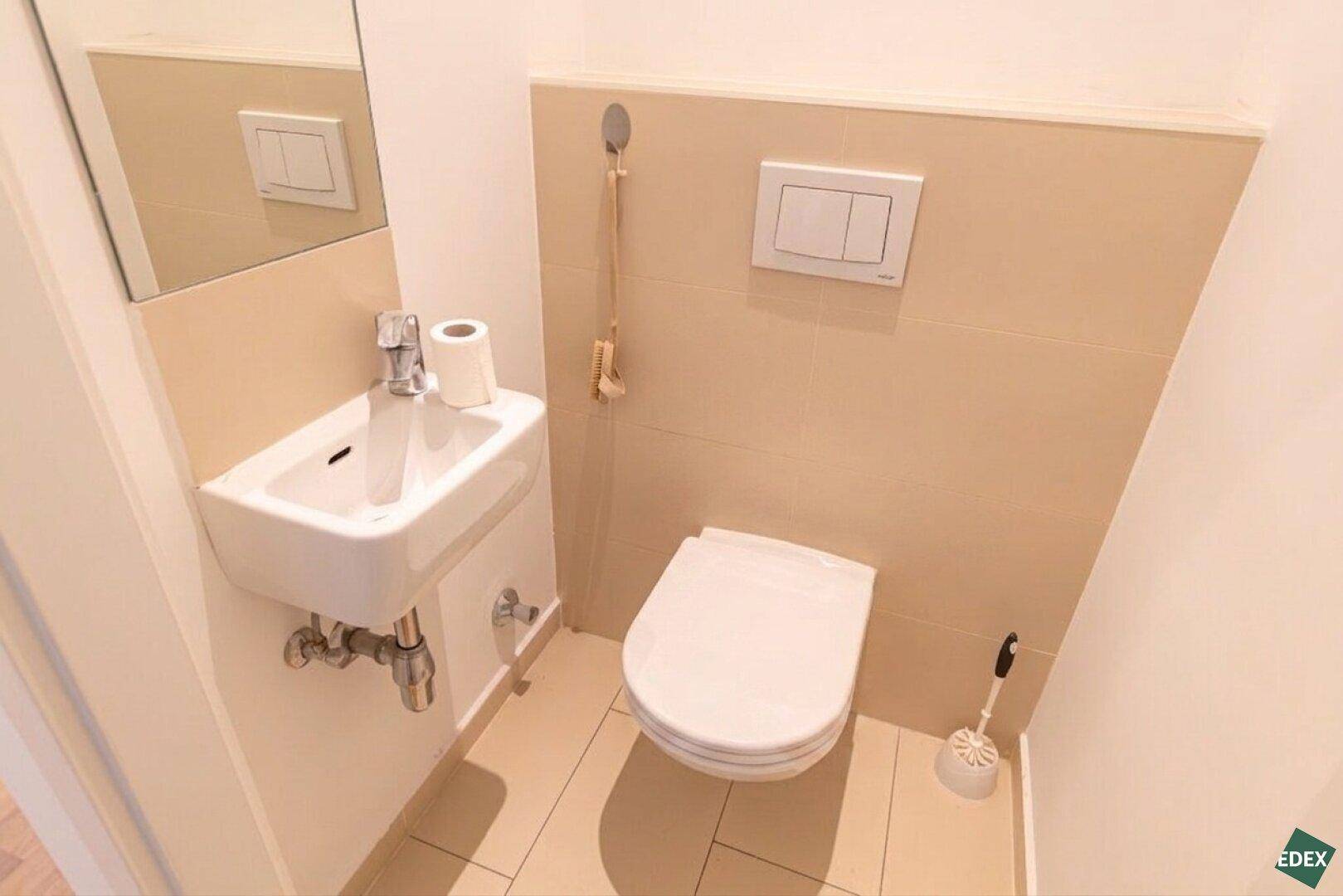 Modernes Gäste-WC mit Wand-WC, kleinem Handwaschbecken und beigefarbenen Fliesen.