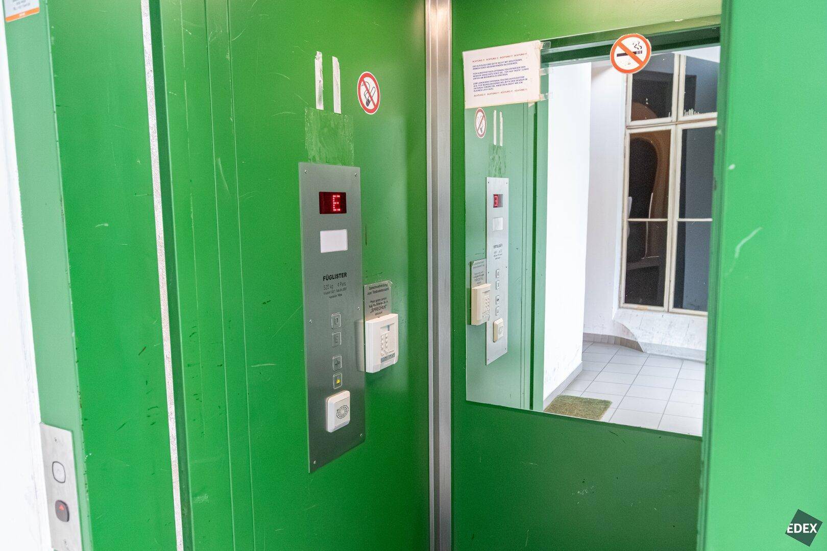 Grüner Aufzug mit Bedienfeld und Spiegel, der Zugang zu den Etagen bietet.