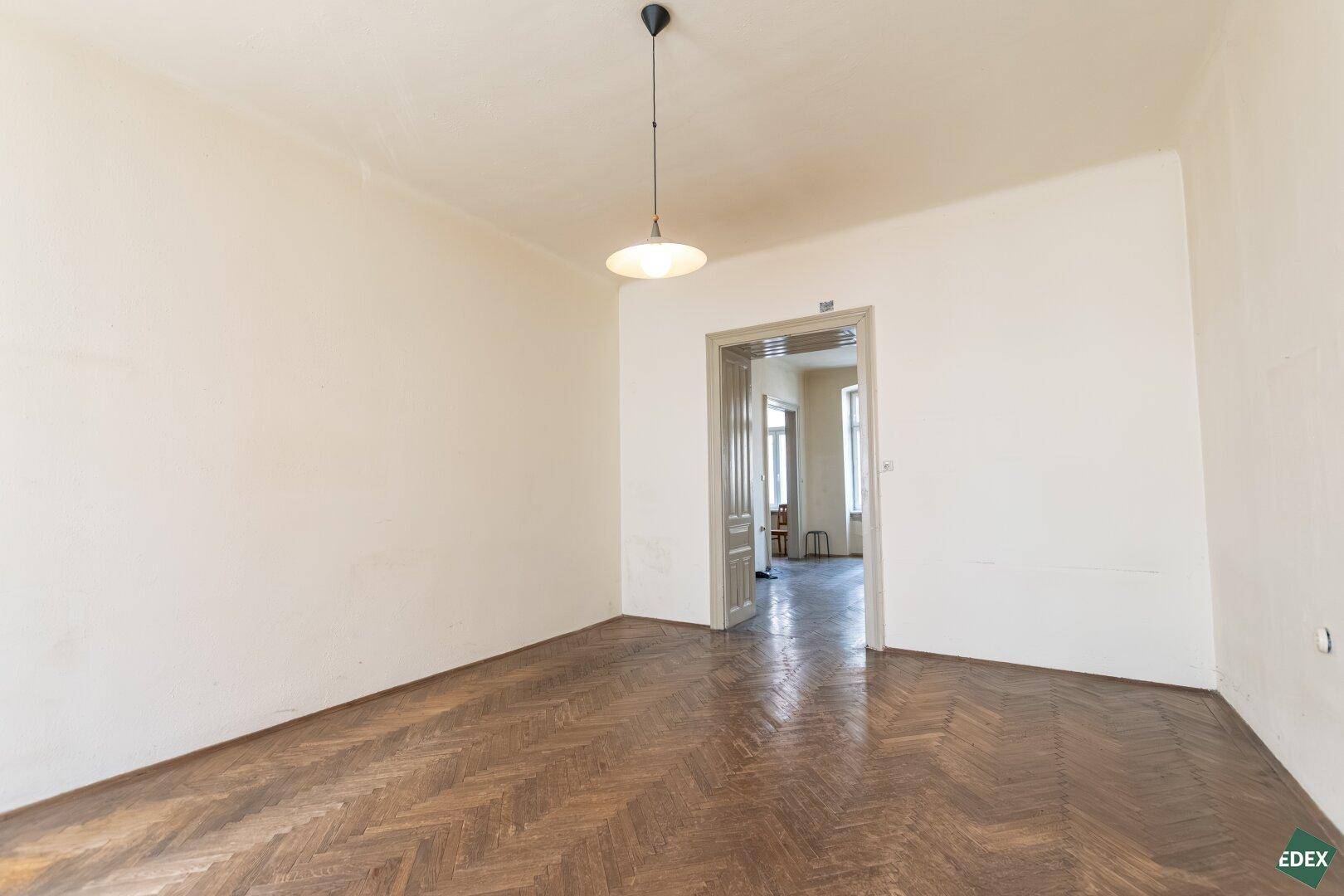 Geräumiges Zimmer mit Fischgrätparkett und Durchgang zu weiteren Räumen.