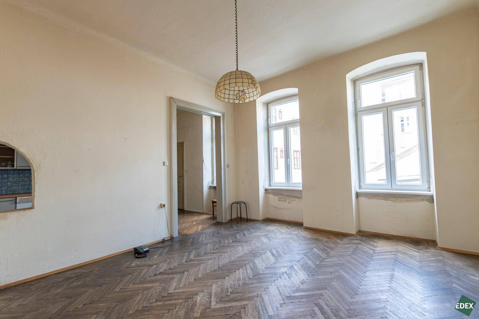 Heller Raum mit Fischgrätparkett, hohen Decken und zwei großen Bogenfenstern.
