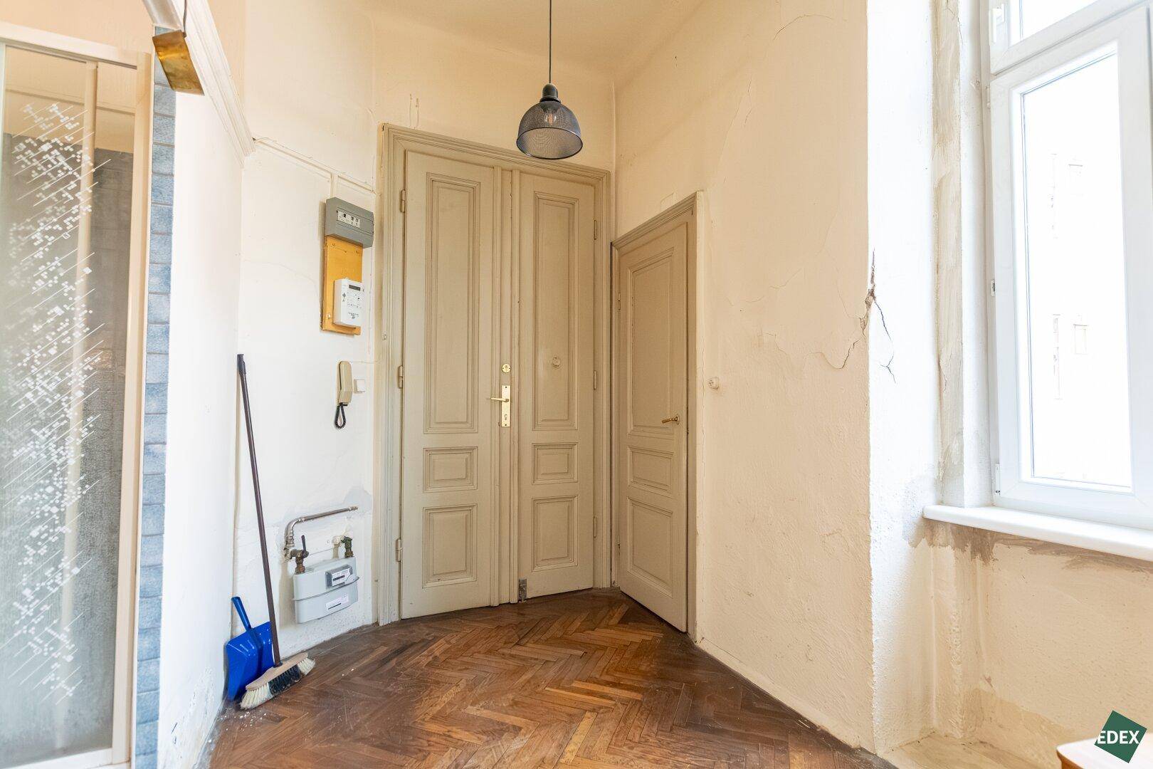 Eingangsbereich mit Fischgrätparkett, Doppeltür und Zählerkasten an der Wand.
