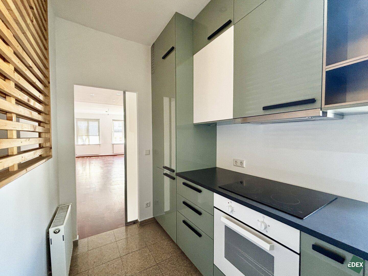 Moderne Küche mit grünen Schränken und Blick in den angrenzenden Wohnbereich.