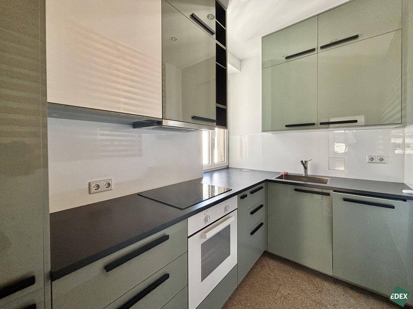 Moderne Küche mit grünen Hochglanzfronten, Induktionskochfeld und Backofen.