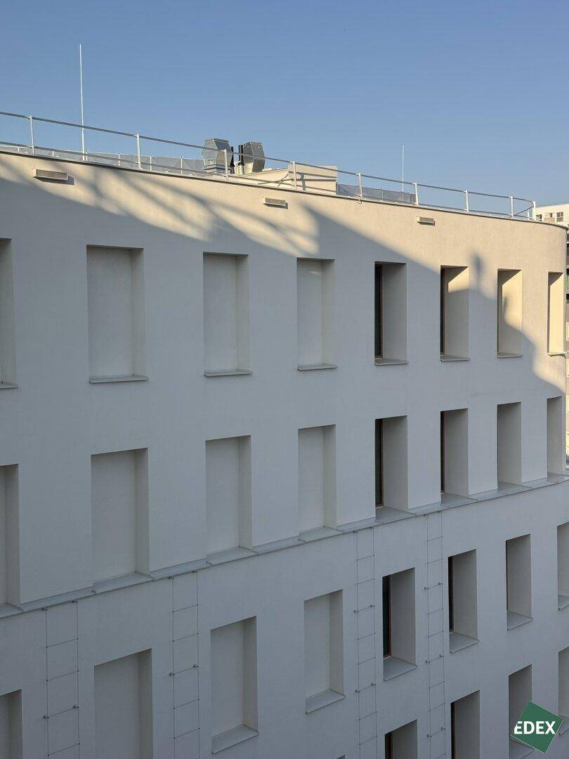 Nahaufnahme einer modernen Gebäudefassade mit vielen Fenstern und klaren Linien unter blauem Himmel.