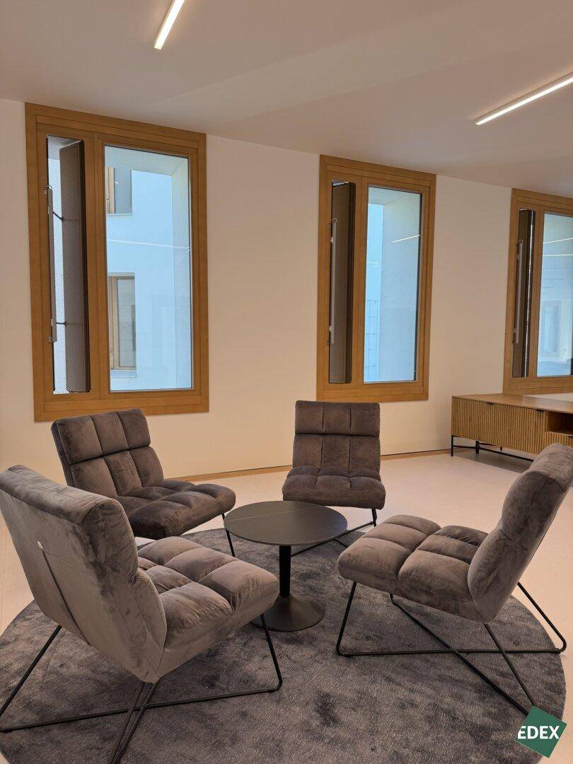 Gemütlicher Loungebereich mit vier modernen, grauen Sesseln und einem runden Teppich vor großen Fenstern.