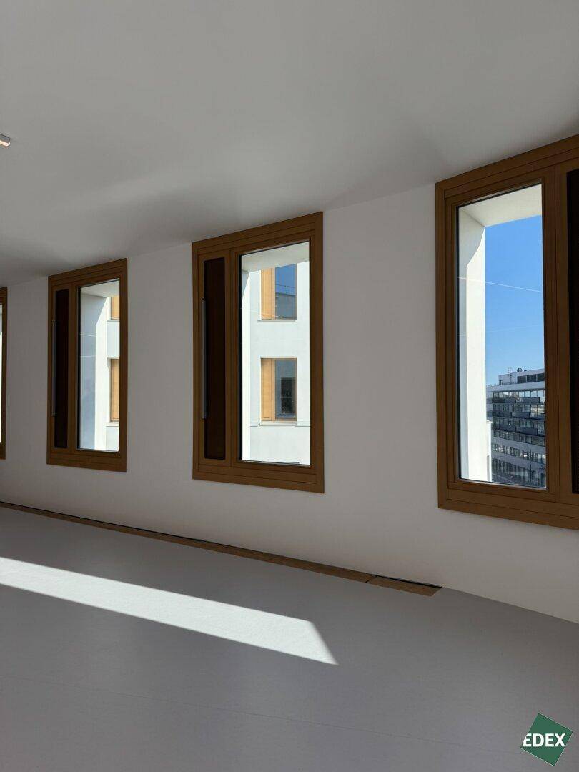 Heller Innenraum mit mehreren großen Fenstern und Blick auf andere moderne Gebäude.