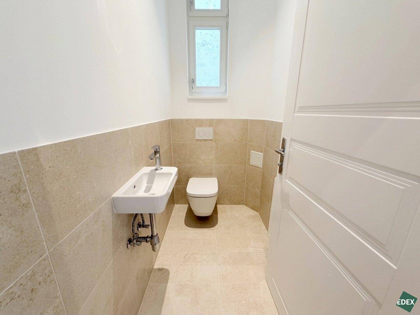 Kleines Gäste-WC mit Fenster, Wand-WC und modernem Handwaschbecken, praktisch und hell gestaltet.