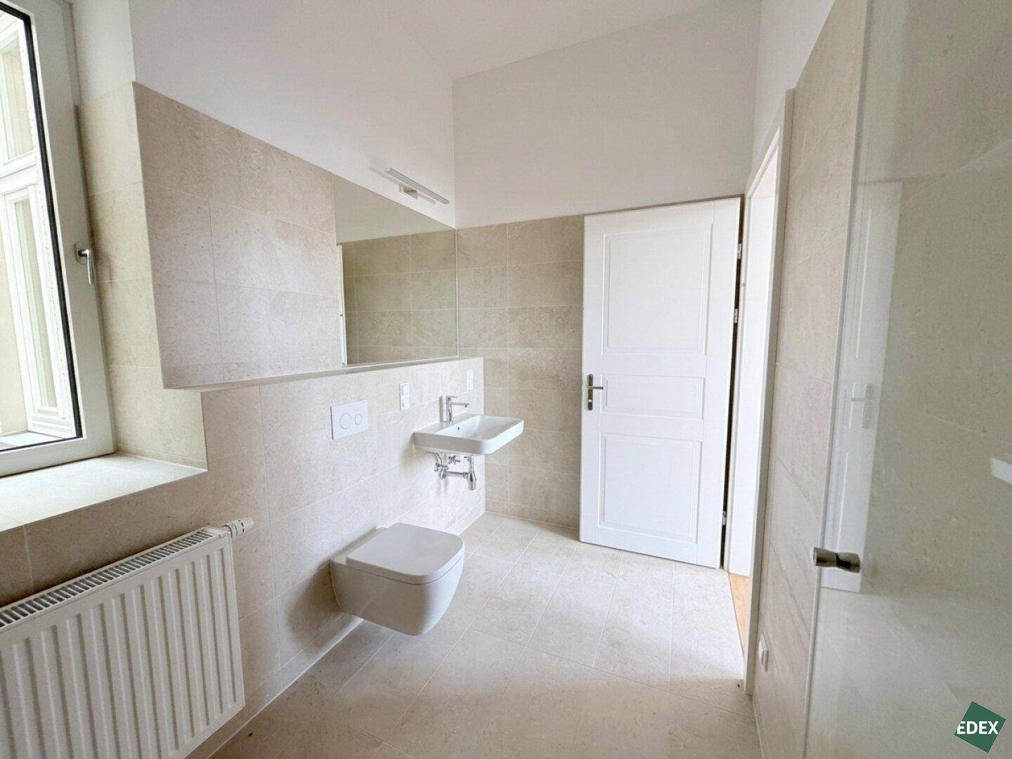 Helles Badezimmer mit modernem Waschtisch, Wand-WC und großem Spiegel, ausgestattet mit beigefarbenen Fliesen.