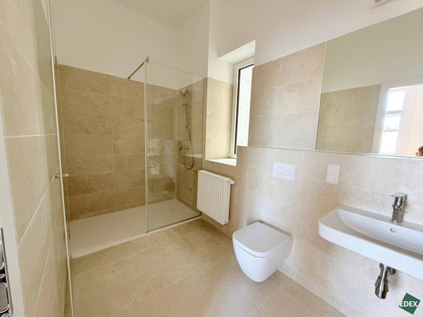 Modernes Badezimmer mit begehbarer Dusche, Wand-WC und beigefarbenen Fliesen, hell und funktional gestaltet.