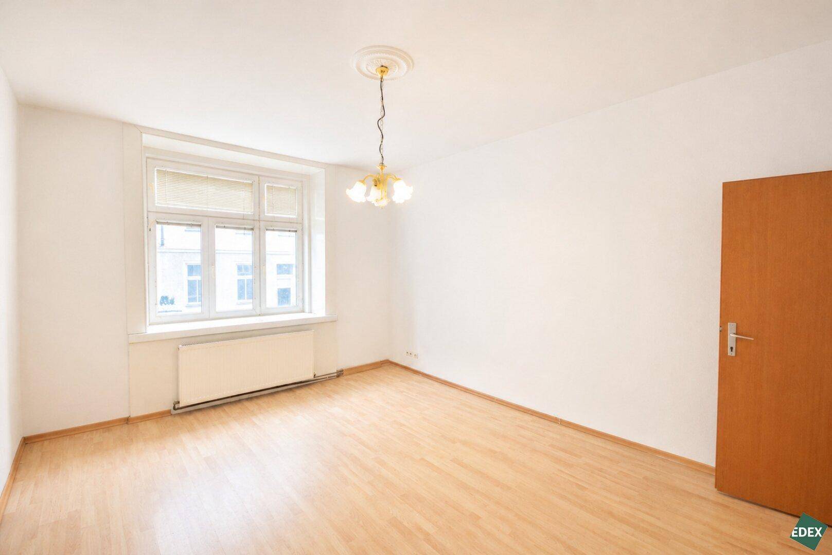 Leeres Zimmer mit hellem Holzboden und großem Fenster, bereit zur individuellen Gestaltung.