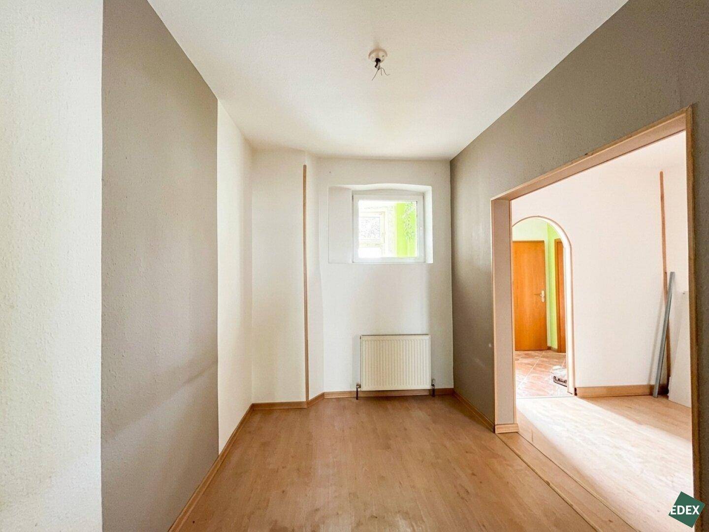 Flur mit Holzboden, kleinerem Fenster und einem Durchgang zu weiteren Räumen.