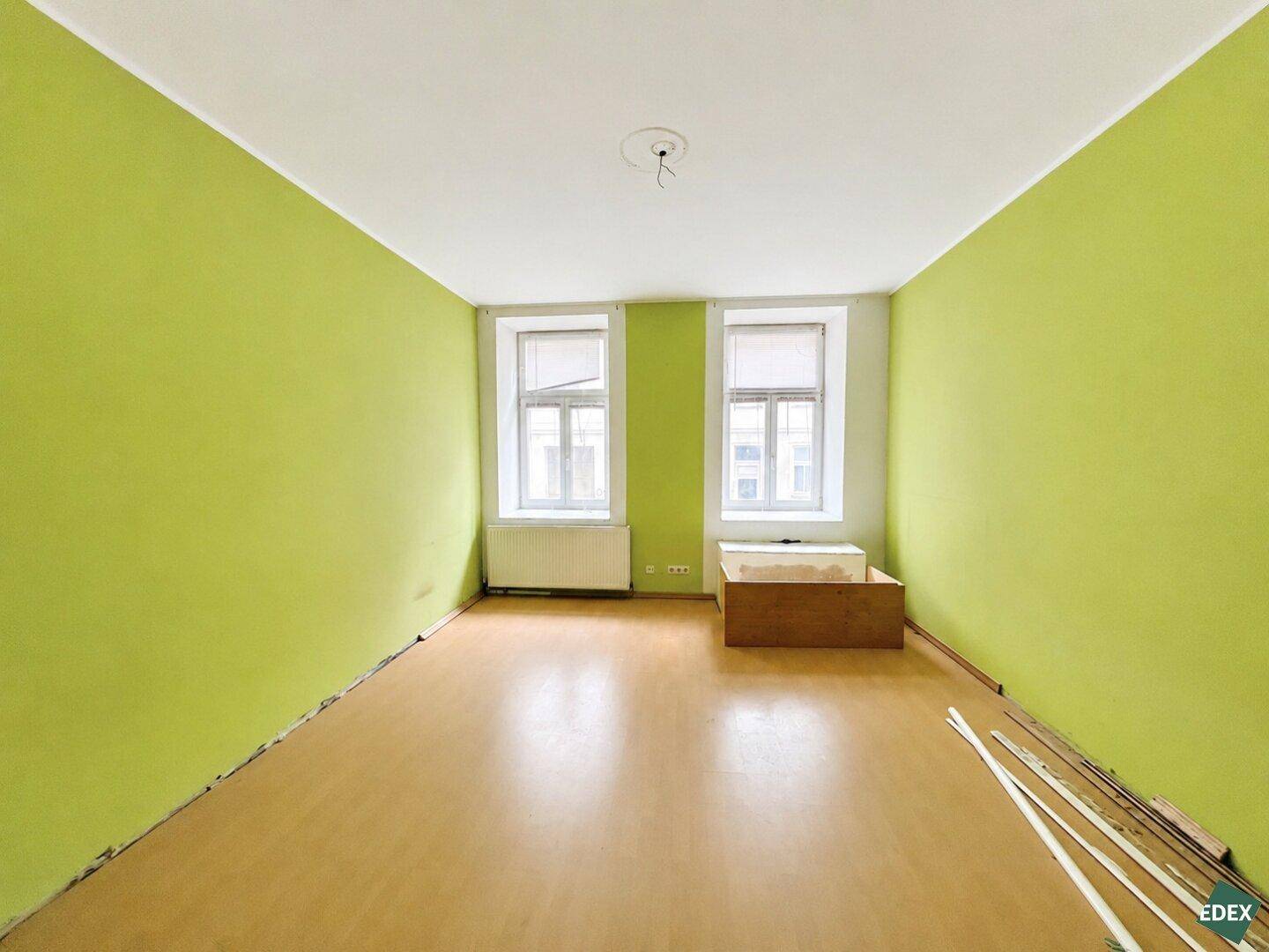 Leeres Zimmer mit auffällig grünen Wänden und hellem Holzboden, ideal für kreative Einrichtung.
