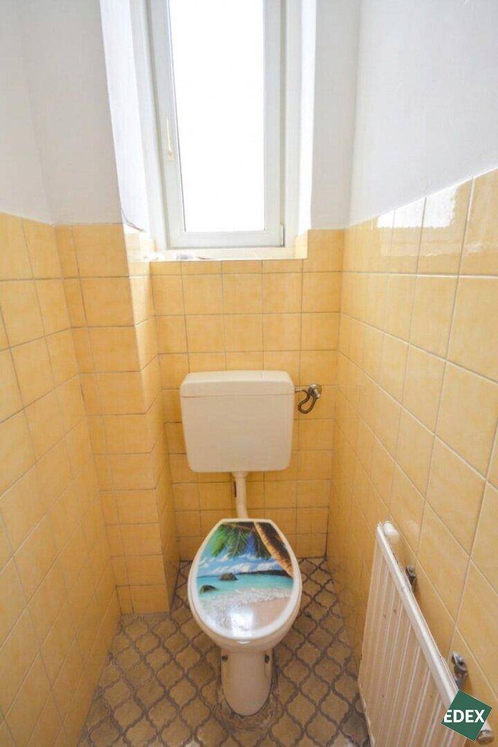 Separate Toilette mit gelben Fliesen, Fenster und einem Heizkörper.