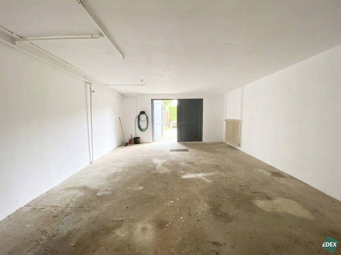 Geräumige, leere Garage mit Betonboden und offenem Tor zum Außenbereich.