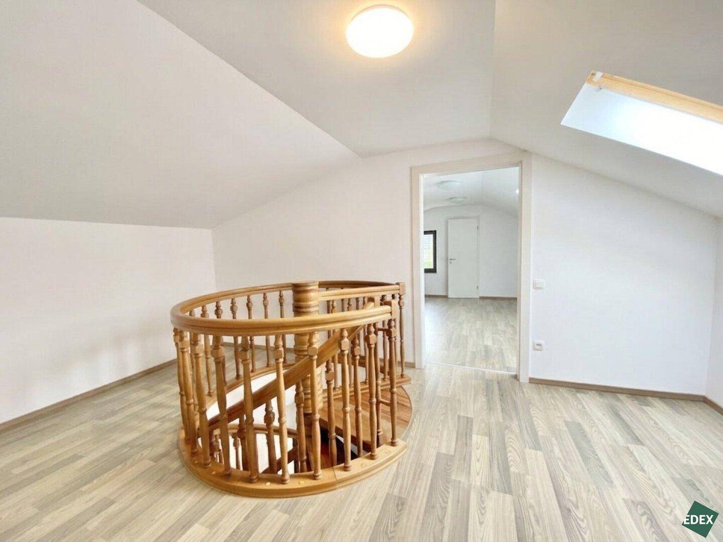 Geräumiger Dachbodenbereich mit Laminatboden, Holzgeländer und Dachfenster.