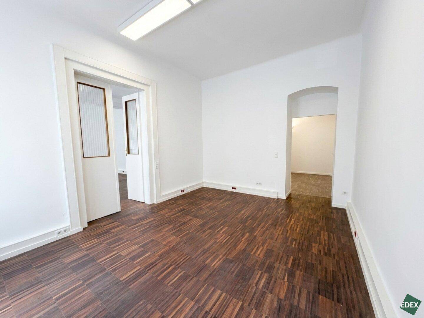Heller Raum mit Parkettboden und Durchgängen zu weiteren Bereichen, ideal für flexible Büronutzung.