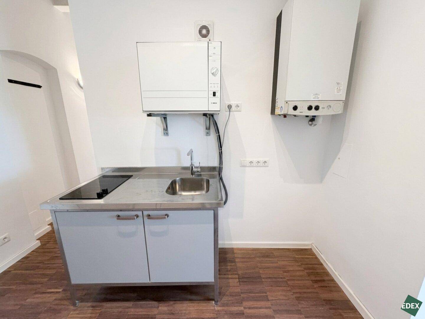 Kompakte Küchenzeile mit Spüle und Kochfeld, ergänzt durch Wandinstallationen und Heizung.