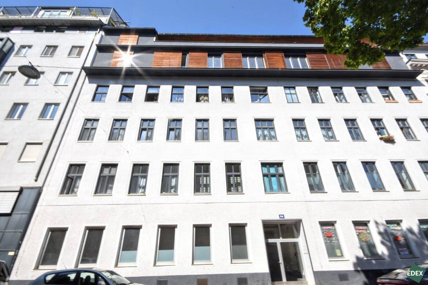Mehrstöckiges Wohngebäude mit vielen Fenstern und moderner Dachkonstruktion unter blauem Himmel.