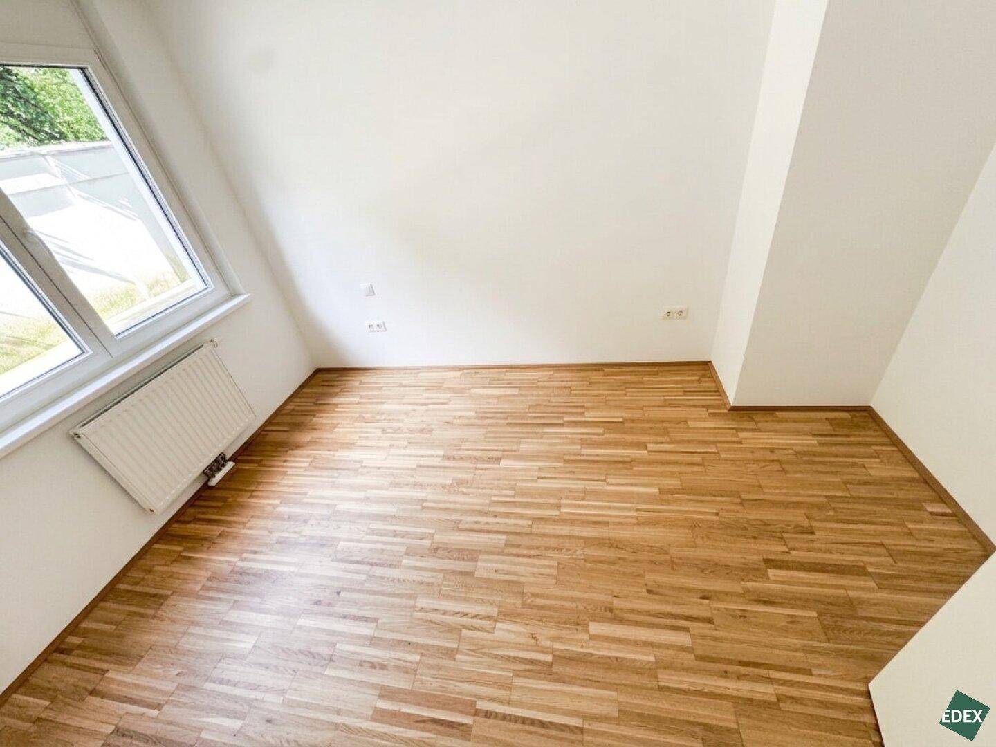 Dachzimmer mit schrägen Wänden, hellem Parkettboden und einem großen Dachfenster für viel Tageslicht.