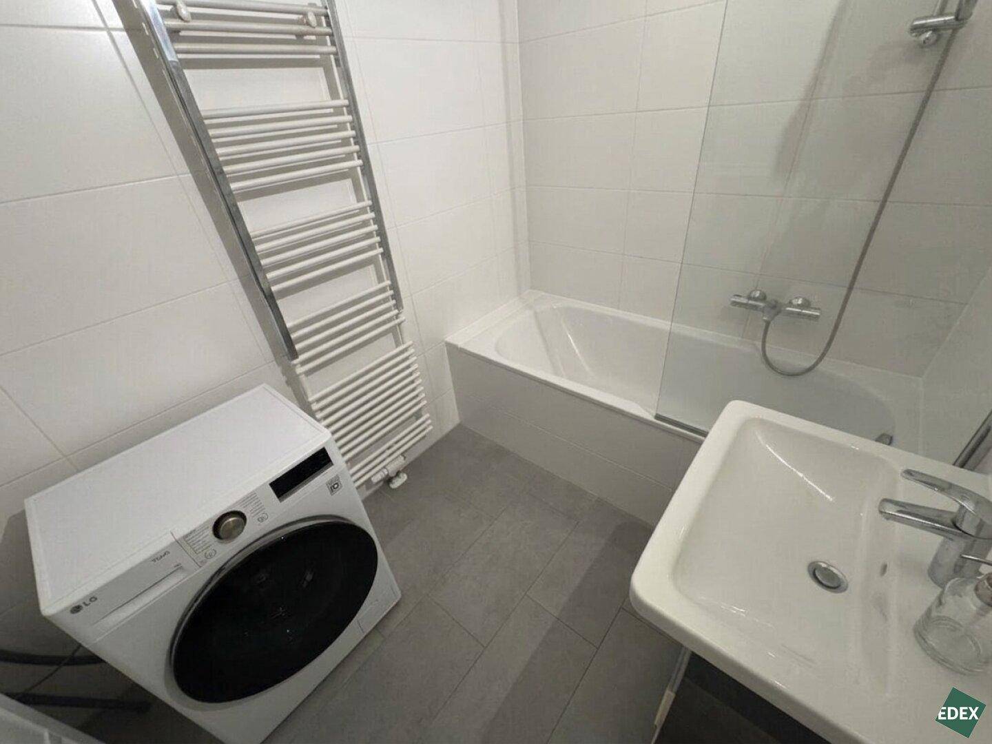 Modernes Badezimmer mit Badewanne, Waschbecken, beheiztem Handtuchhalter und einer Waschmaschine.