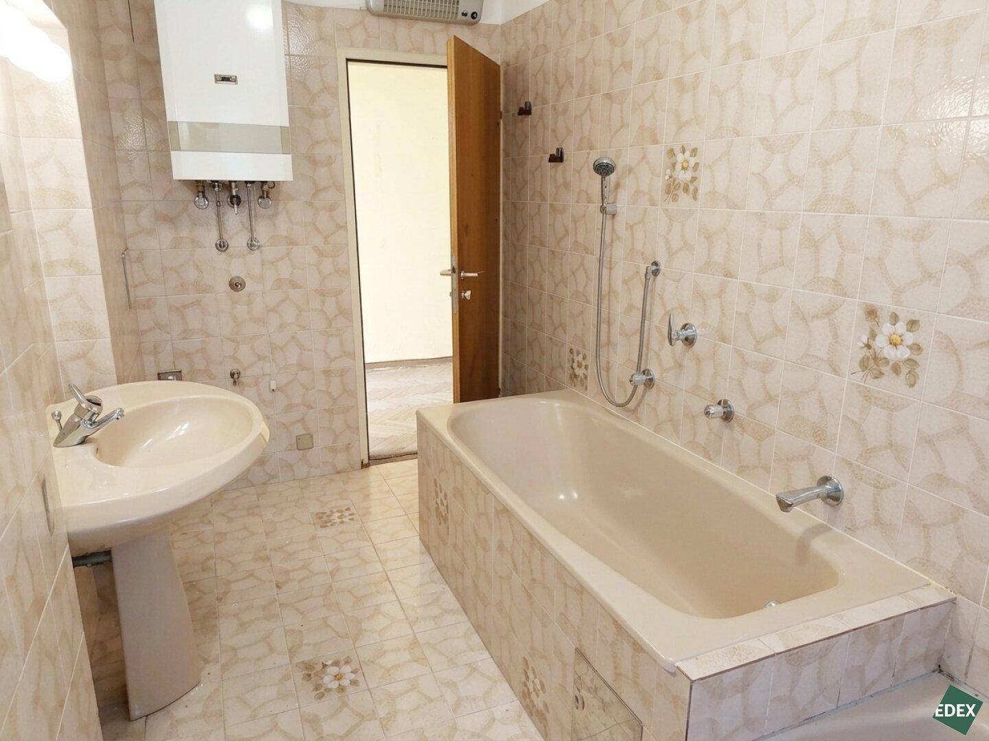 Badezimmer im Stil der 80er Jahre mit beigefarbenen Fliesen, Badewanne und Waschbecken.