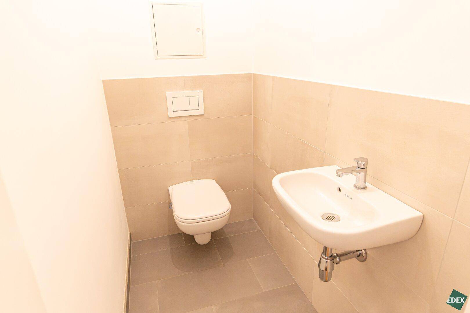 Separates WC mit wandhängender Toilette und kleinem Waschbecken, in hellen Farbtönen gehalten.