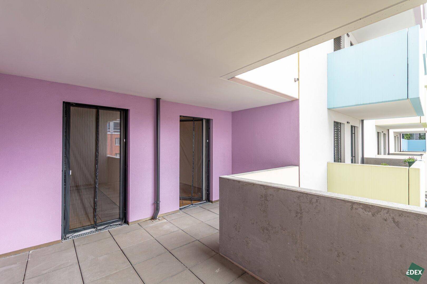 Geräumiger Balkon mit lila Wänden und Fliesenboden, zugänglich von mehreren Zimmern.