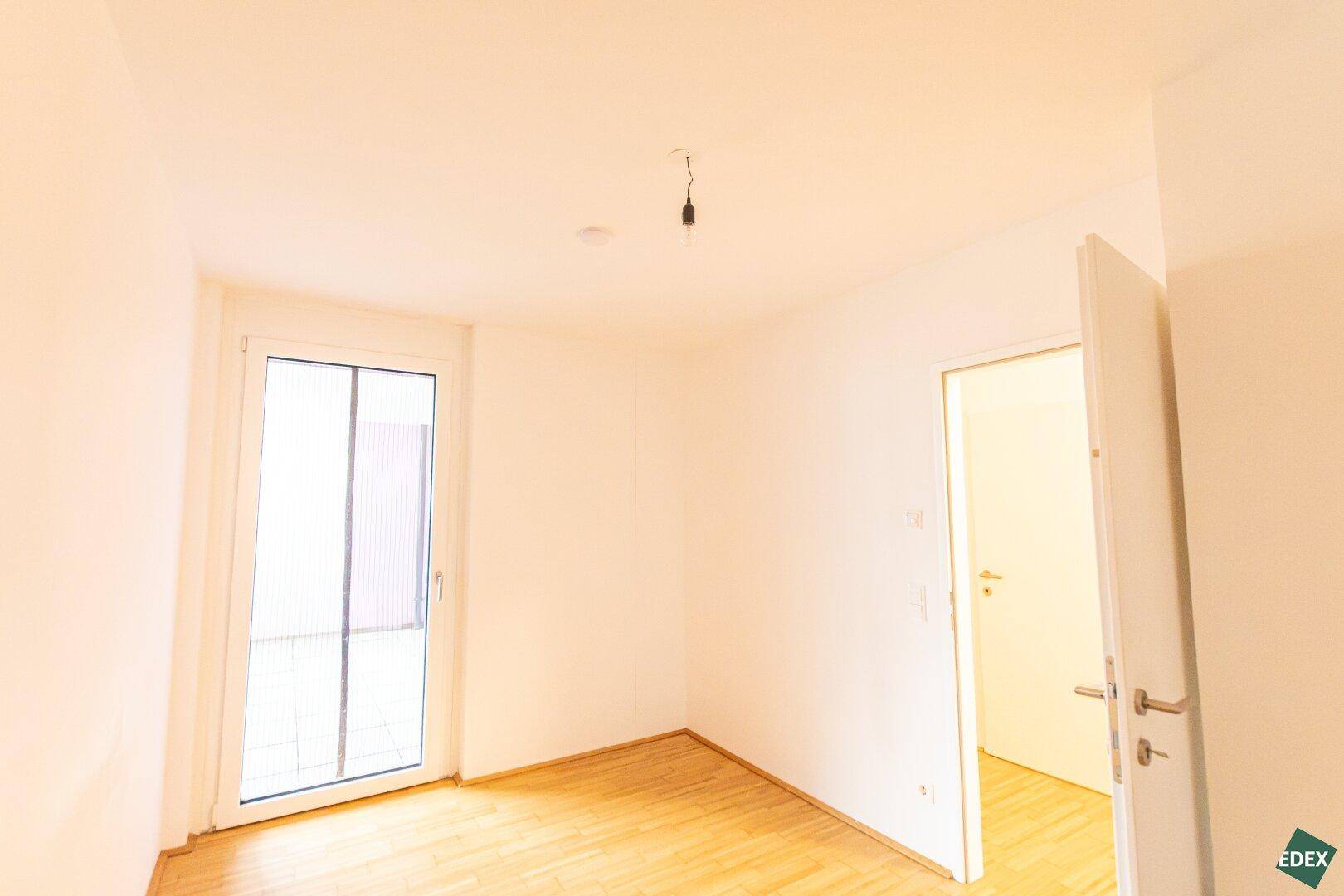 Geräumiges Schlafzimmer mit Parkettboden und viel Tageslicht, angrenzend an ein Badezimmer.