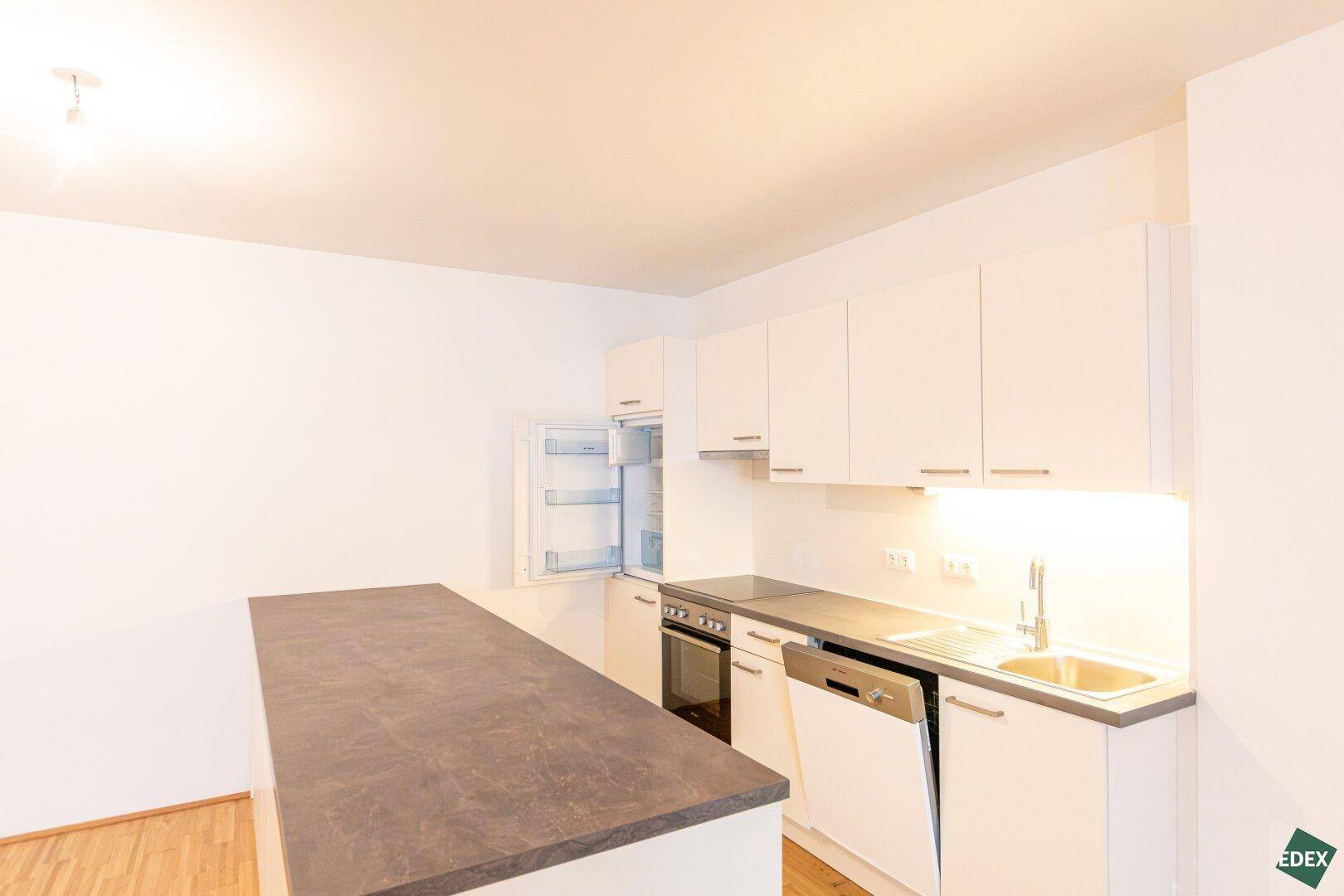 Moderne Einbauküche mit weißen Schränken, dunkler Arbeitsplatte und integrierten Geräten.