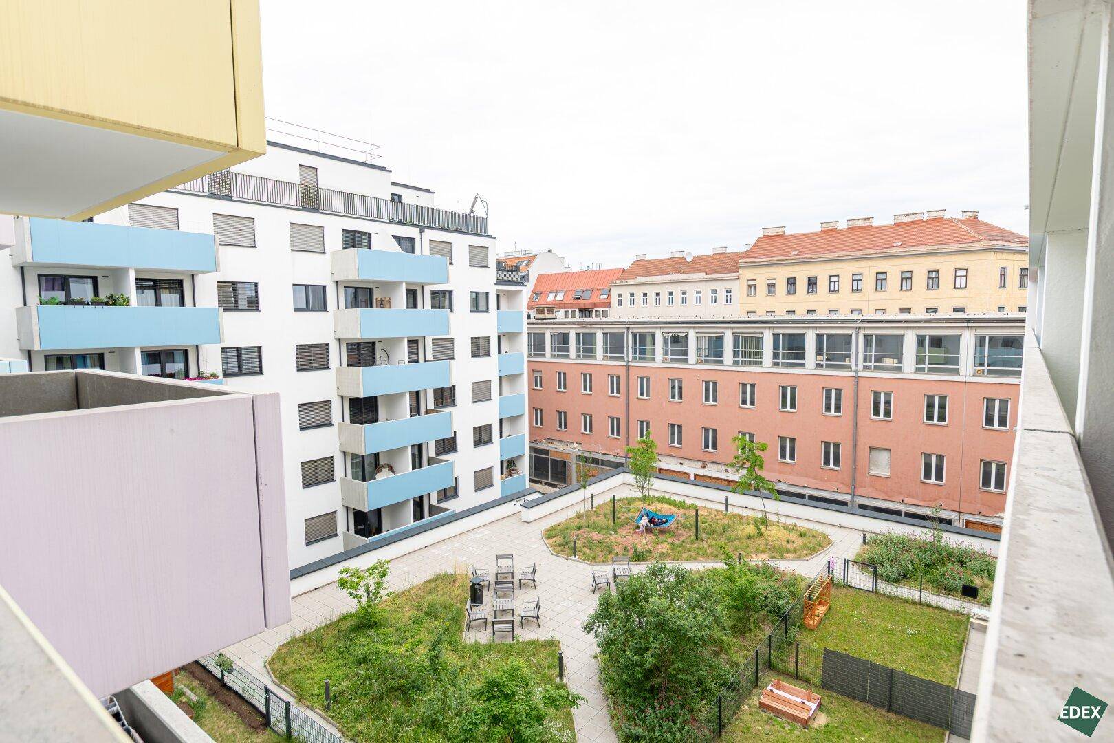Panoramablick auf den gepflegten Innenhof mit Spielplatz und Sitzbereichen, umgeben von Wohngebäuden.
