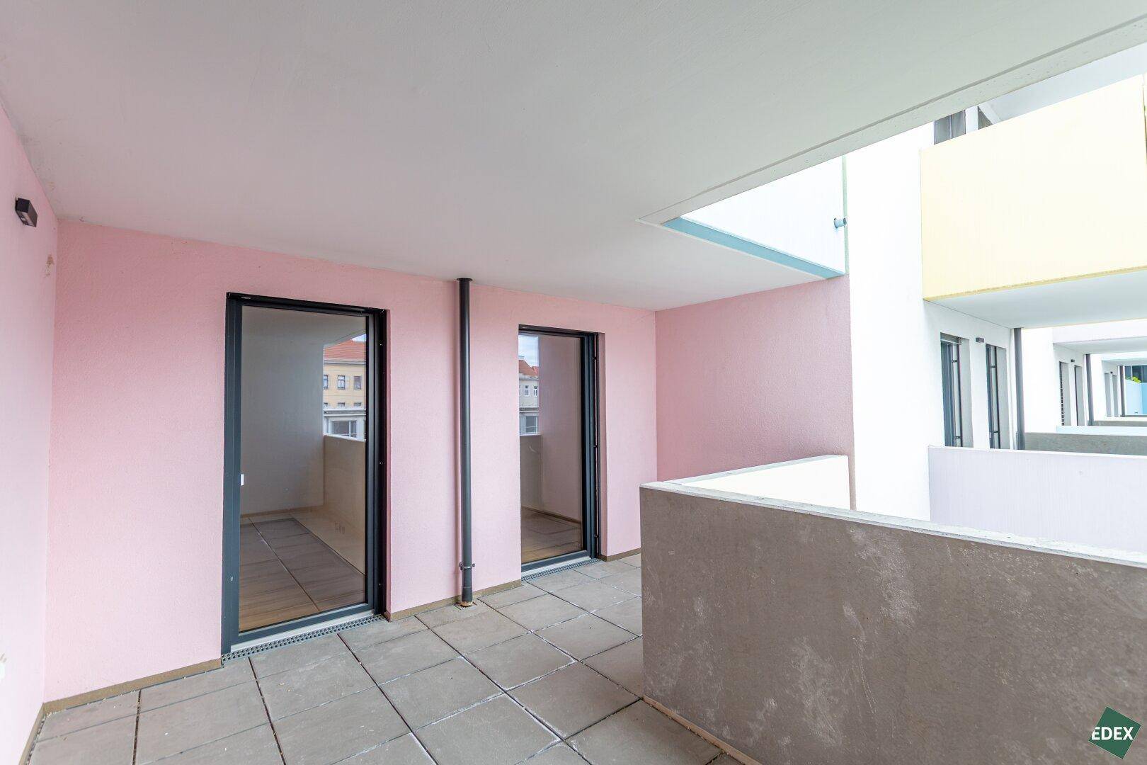 Geräumige Terrasse mit rosafarbenen Wänden und Fliesenboden, bietet Platz für Entspannung im Freien.