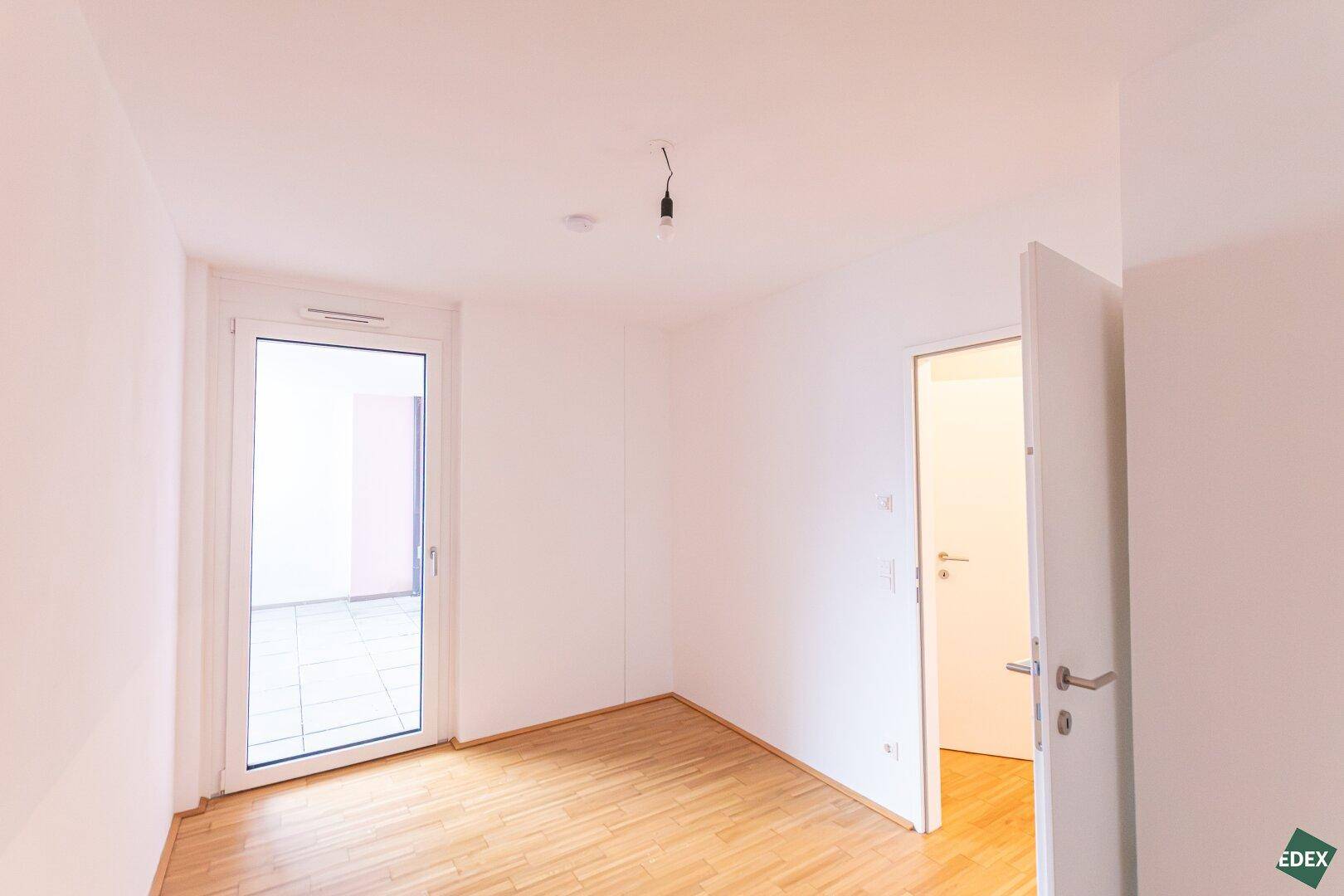 Geräumiges Zimmer mit Holzboden und Zugang zum Außenbereich, ideal als Schlafzimmer oder Arbeitszimmer.