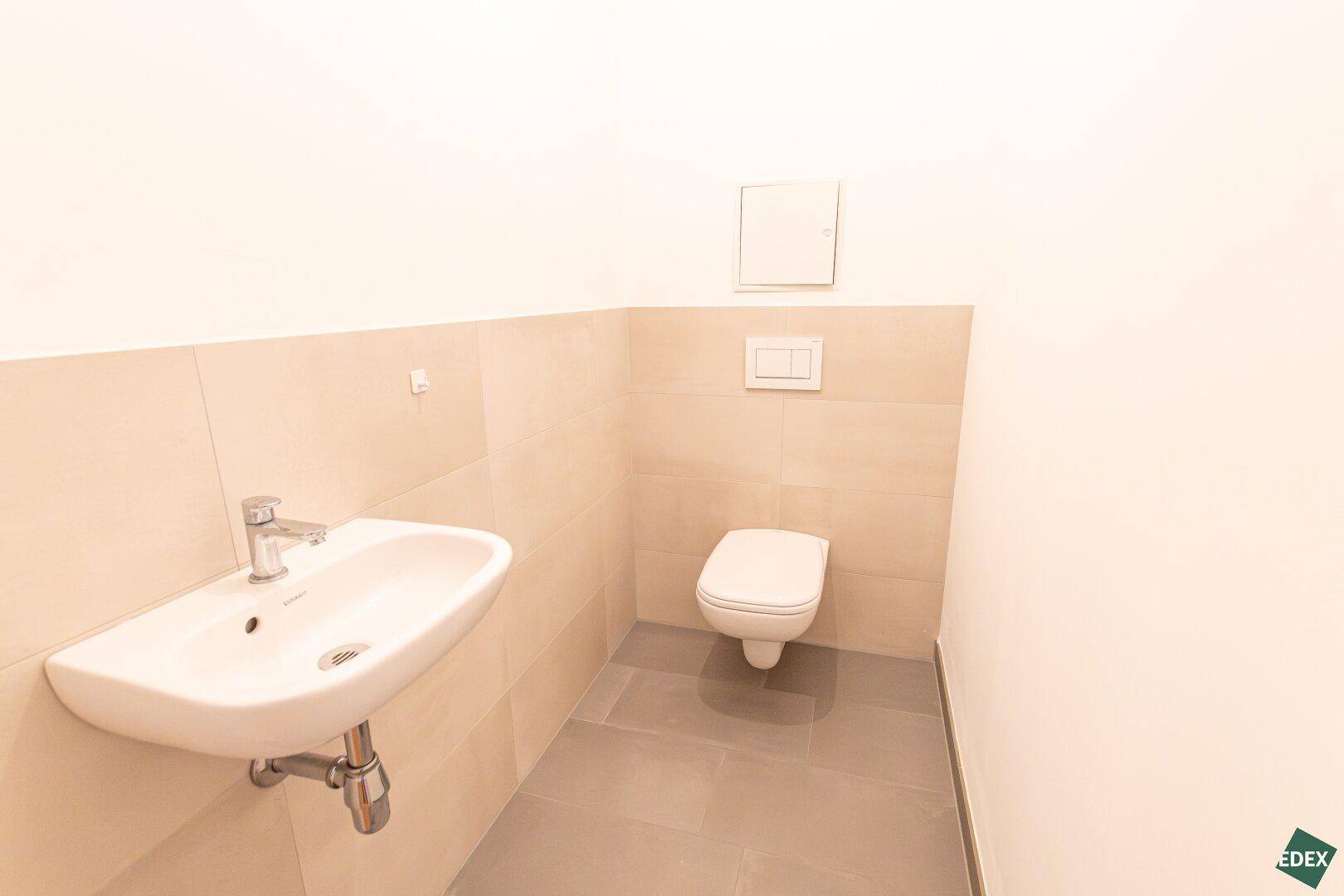 Separates Gäste-WC mit wandhängender Toilette und kleinem Waschbecken, in neutralen Farbtönen gehalten.