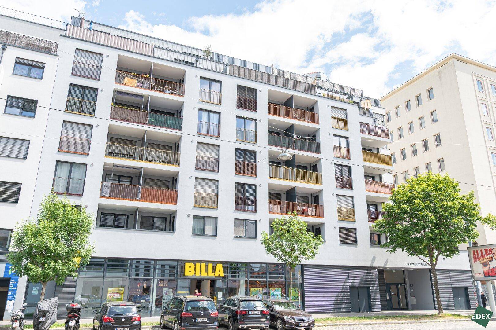 Moderne Gebäudefassade mit Balkonen und einem Supermarkt im Erdgeschoss an einer belebten Straße.