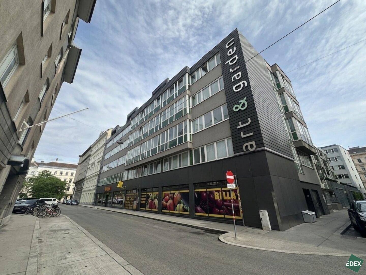 Modernes Geschäftsgebäude an einer Straßenecke mit großen Fenstern und Einzelhandelsflächen im Erdgeschoss.