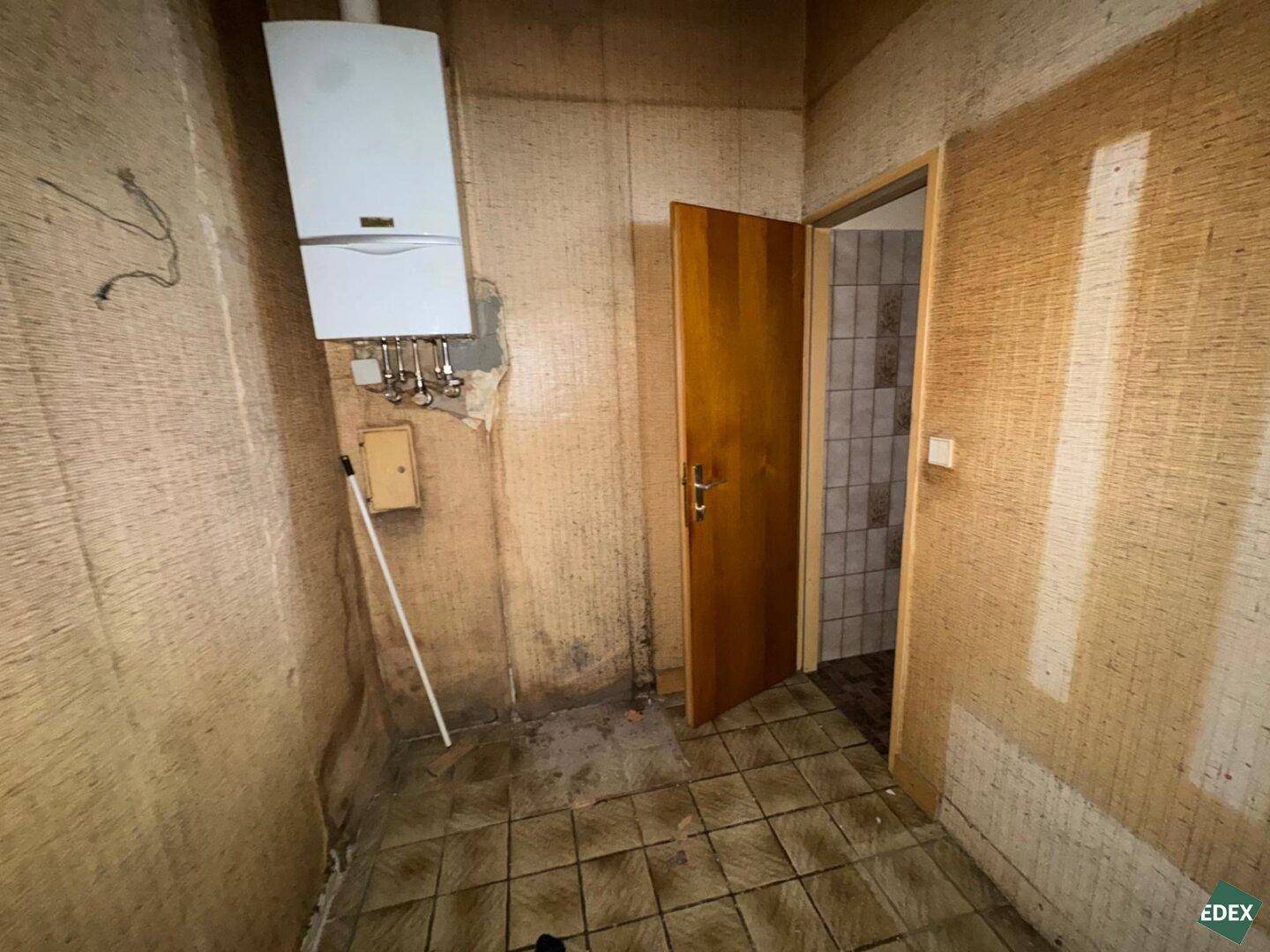 Kleiner Raum mit Gastherme an der Wand, Fliesenboden und Zugang zu einem weiteren Zimmer.