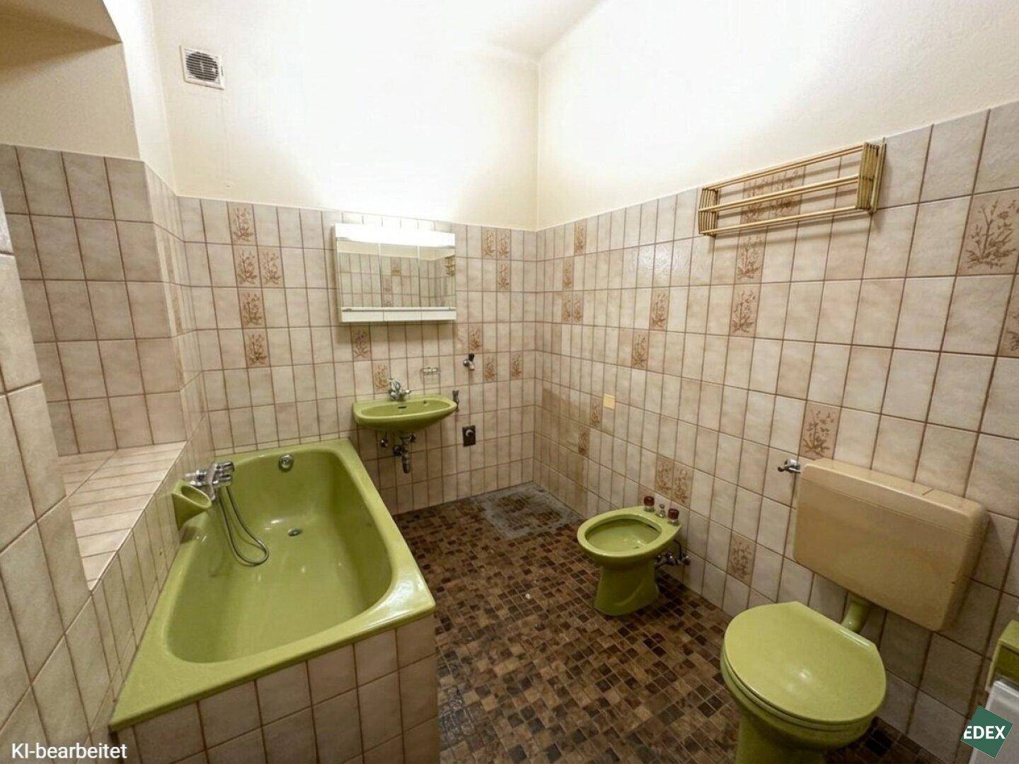 Veraltetes Badezimmer mit grüner Badewanne, Toilette, Bidet und gemusterten Fliesen.